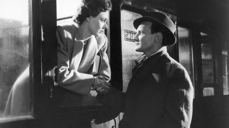 A still from the black and white movie Brief Encounter of a woman leaning out of a train window towards a man
