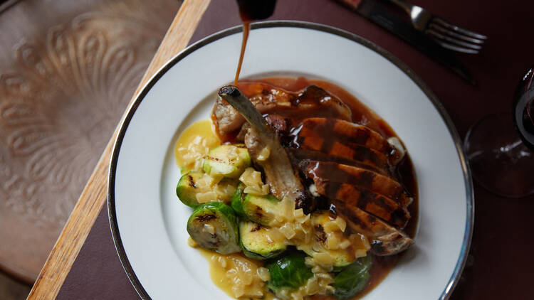 A white plate piled high with meat and vegetables on a table, with gravy being poured onto the meat