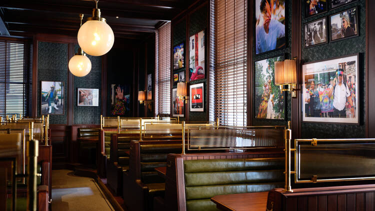 A row of booths with dark wooden tables and green leather-backed seating at Side Hustle