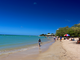 A bright day at Combate Beach with a person strolling near the water on the white sand